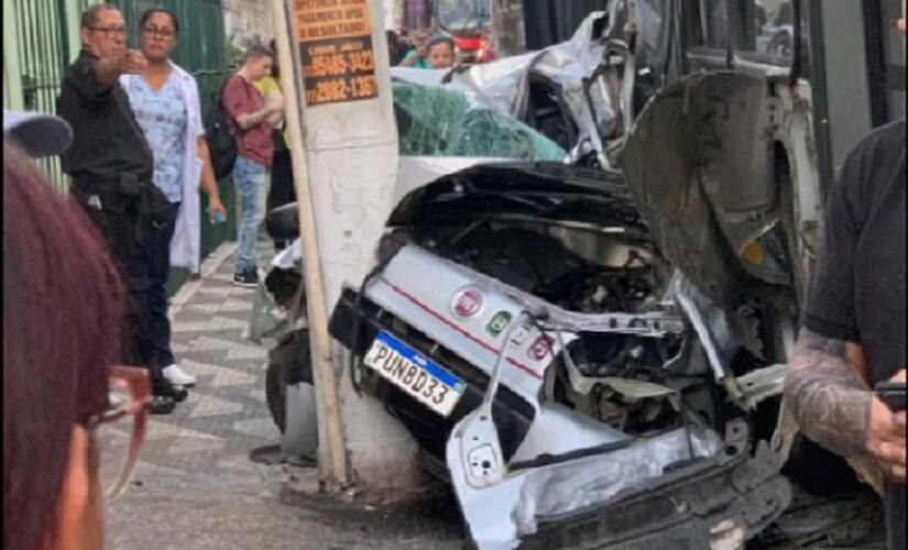 Veículo ficou esmagado entre o poste e o ônibus