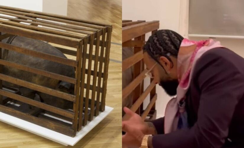 Jogador se agacha em frente à obra e faz um gesto de lamentação com as mãos, em tom irônico
