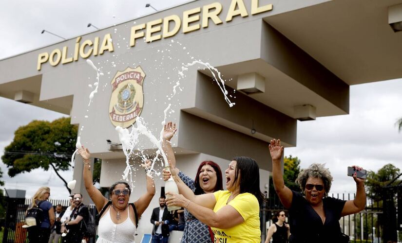 Três mulheres (uma com uma camiseta estampada com a frase "lava tua alma Brasil") estouraram um champanhe em frente à entrada