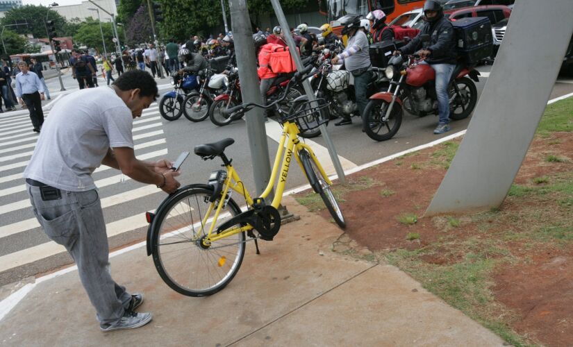 Usuário destrava bicicleta da Yellow com o seu celular na avenida  Brigadeiro Faria Lima na esquina com a avenida Rebouças