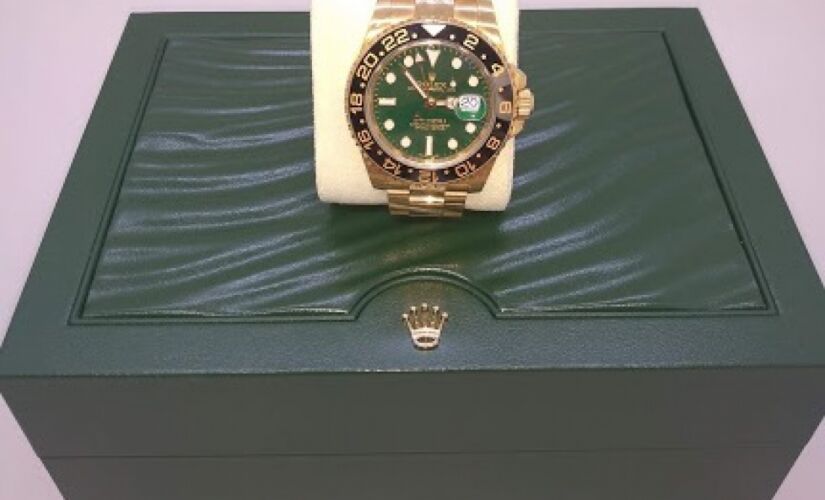 O item com o maior lance inicial é um relógio de pulso da marca Rolex, modelo GMT-Master II, com pulseira de ouro amarelo 18k