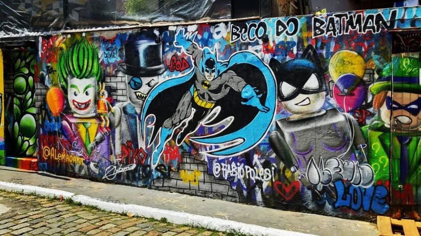 O nome do local vem de um grafite do personagem Batman, da DC Comics, que apareceu nos muros do bairro em 1980. Desde então, o Beco tem sido coberto por várias obras de arte, incluindo influências cubistas e psicodélicas, transformando-o em uma espécie de galeria ao ar livre. / Foto: Instagram/@becodobatman.oficial 