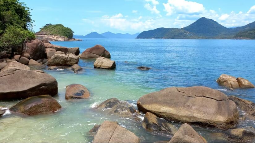 O acesso à Ilha do Prumirim se dá a partir da Praia do Prumirim, um local igualmente encantador com uma faixa de areia ampla e mar de tombo. A praia oferece ótimos quiosques e uma vista privilegiada da ilha, sendo o ponto de partida para os barcos que fazem a travessia. Foto: Divulgação/Caminho das Trilhas