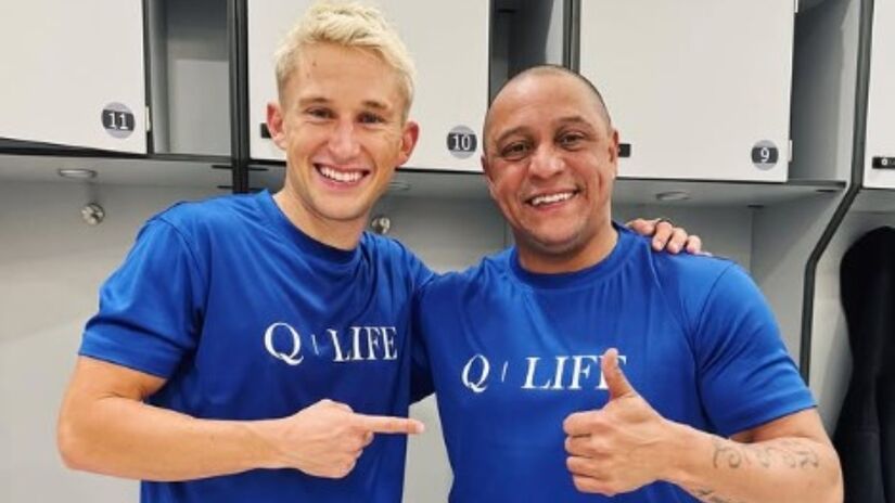 Anders ao lado de Roberto Carlos em vestiário de jogo festivo.
