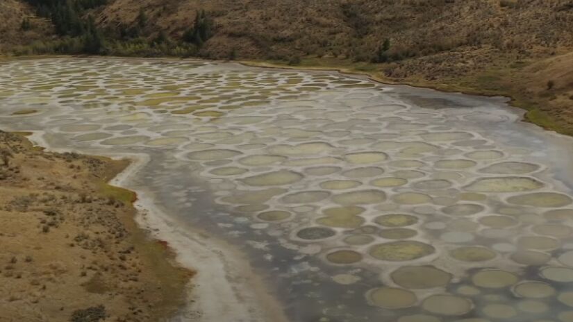 Spotted Lake - Canadá: Mais um lago canadense na lista, este se destaca pelas bolhas gigantes. Durante o verão, a água evapora e acaba contribuindo para a formação de poças ricas em minerais como magnésio, cálcio, e sulfato de sódio, criando manchas circulares de tons variados - (Reprodução/YouTube)