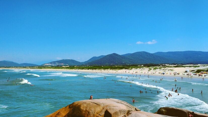 A Praia da Joaquina, por exemplo, é famosa entre surfistas por suas ondas perfeitas, enquanto a Lagoa da Conceição é um destino ideal para esportes aquáticos e passeios relaxantes. Foto: Wikimedia Commons