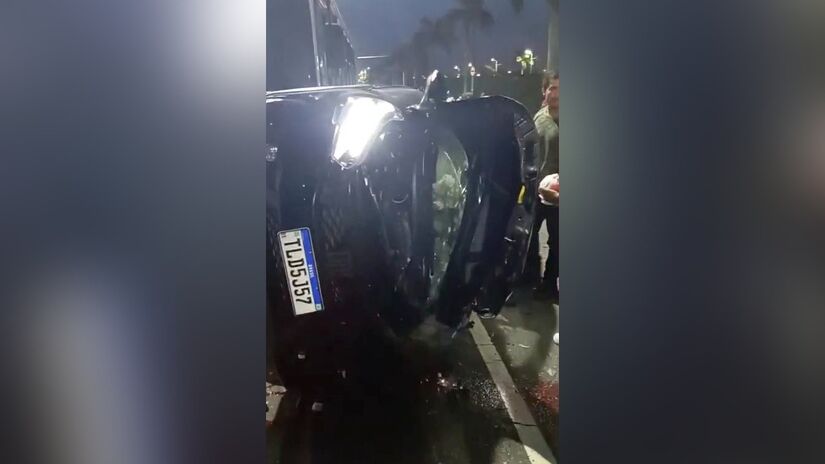 O carro em que o ex-delegado estava bateu em um ônibus e tombou ao fugir dos criminosos. Em seguida, homens com máscara e colete à prova de balas descem do carro que o perseguiam e o executam com cerca de 20 tiros de fuzil / Reprodução