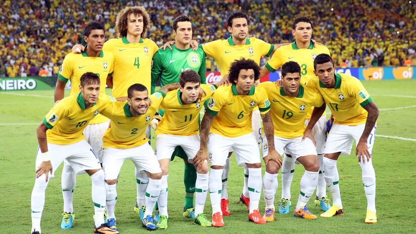 Jogadores da Seleção Brasileira durante partida oficial, em campo diante de estádio lotado. A imagem representa o principal produto esportivo que movimenta receitas milionárias com direitos de transmissão e patrocínios.