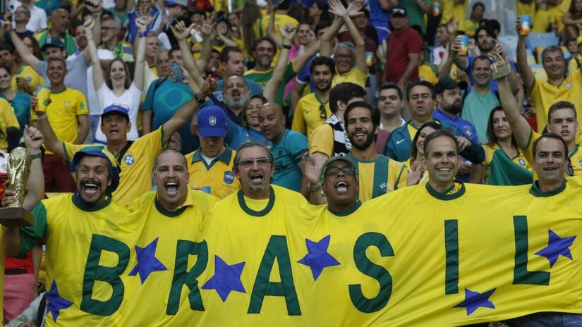 Torcedores da Seleção exibem bandeiras e camisas nas arquibancadas. O engajamento da torcida impulsiona vendas de produtos licenciados, um dos pilares de arrecadação da entidade. Fotos: Wikimedia Commons