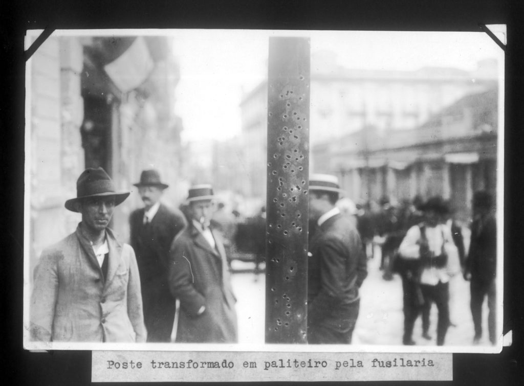 Transeuntes perto de poste atingido por balas de fuzil, durante a Revolução de 1924.