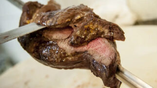 Uma peça de picanha sendo cortada no espeto