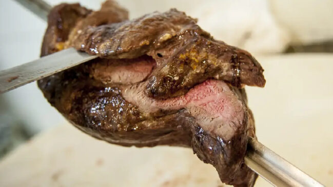 Uma peça de picanha sendo cortada no espeto
