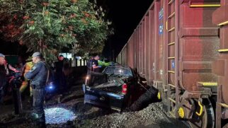 Carro destruído após ser atingido por um trem em passagem de nível em Itirapina (SP); policiais e equipes de resgate atendem a ocorrência durante a noite