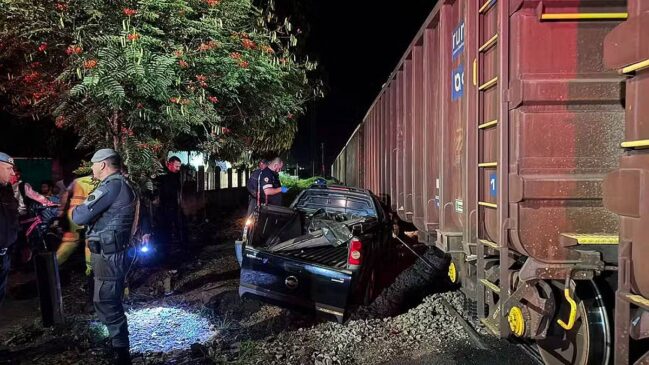 Carro destruído após ser atingido por um trem em passagem de nível em Itirapina (SP); policiais e equipes de resgate atendem a ocorrência durante a noite
