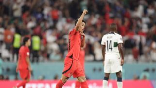 Jogador da Coreia do Sul em jogo da Copa do Catar de 2022, em campo, com jogador de Portugal ao fundo da imagem