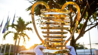 Taça da Copa do Nordeste sendo erguida por mãos com luva branca. Ao fundo Sol e algumas árvores