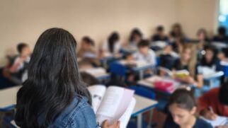 Professora, em primeiro plano, lê parar alunos em uma sala de aula. Minas Gerais anuncia histórico escolar por e-mail