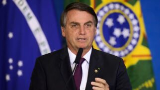 Bolsonaro discursando com bandeira ao fundo