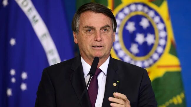 Bolsonaro discursando com bandeira ao fundo