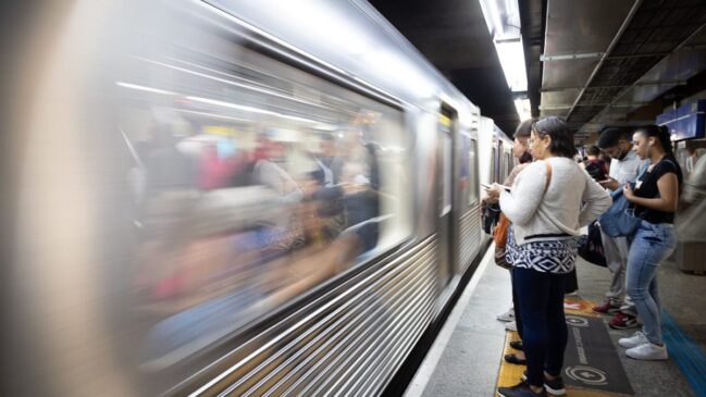 Passageiros aguardam na plataforma do Metrô de São Paulo enquanto um trem passa pela estação