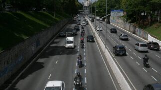 Avenida com fila de motoboys na faixa azul e poucos carros em ambos sentidos