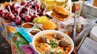 Mesa com comidas típicas de festa junina expostas; há maçã do amor, pão com carne louca e marmita com arroz e almôndegas.