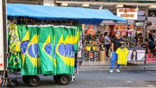 Tenda de venda de camisetas e artigos da seleção brasileira à esquerda da imagem. Do outro lado, um comerciante segura uma camiseta do Brasil à venda.