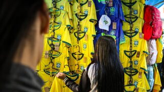 Camisas do Brasil expostas na 25 de março durante o dia. Garota observa produtos