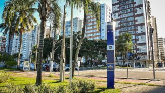 Rua com prédios residenciais e palmeiras ao lado de equipamento de monitoramento urbano instalado em calçada