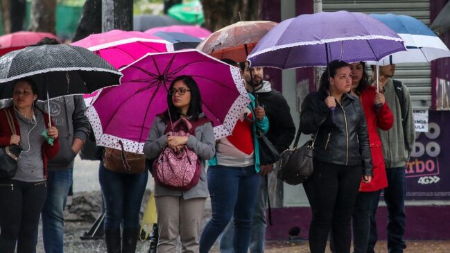 Pessoas caminham com guarda-chuvas e casacos em dia de chuva na cidade de São Paulo.