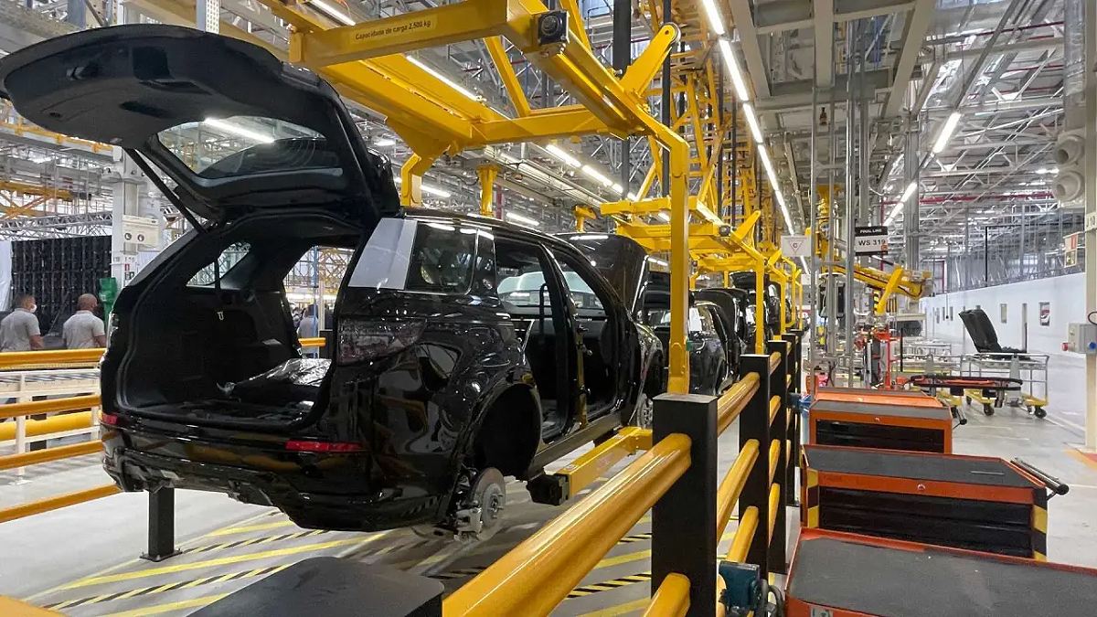 Linha de produção de veículos em fábrica automotiva, com carros em fase de montagem e equipamentos industriais ao redor