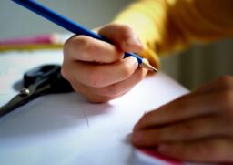 Criança em idade escolar escrevendo em papel com lápis