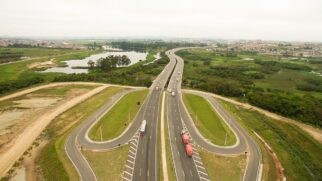 Vista aérea ampla e centralizada de um trecho duplicado do Rodoanel Mário Covas. Em primeiro plano, destacam-se duas grandes alças de acesso asfálticas em formato de "U" invertido nas laterais da pista principal.