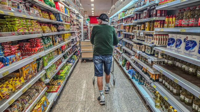 Idoso caminhando em corredor de supermercado para comprar cestas básicas em SP
