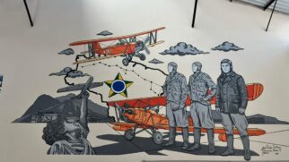 Pintura mural em uma parede branca retratando elementos da história da aviação militar