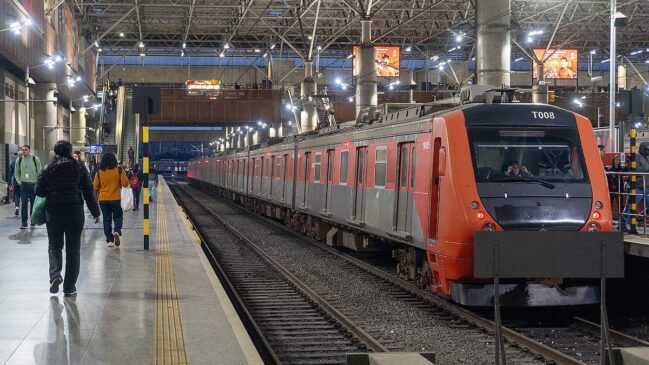 Fotografia em ângulo de três quartos de um trem da CPTM nas cores vermelha e cinza, parado ao lado da plataforma de uma estação coberta de grande porte. Na cabine frontal vermelha, vê-se a identificação "T008" no topo e o número "9005" na lateral.