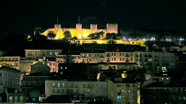 Castelo de São Jorge se destaca iluminado sobre os telhados de Lisboa durante a noite, no alto de uma das colinas da capital portuguesa (Foto: LBM1948/Wikimedia Commons)