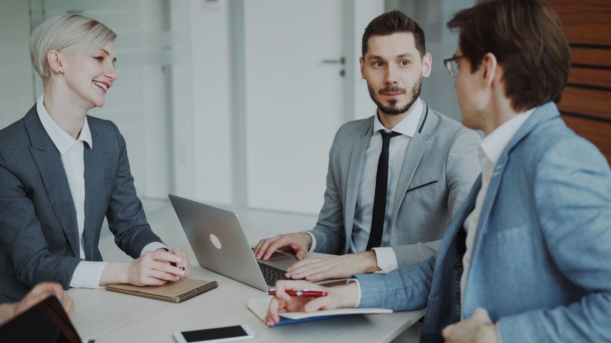 Três advogados conversam em um ambiente profissional enquanto analisam informações relacionadas ao trabalho.