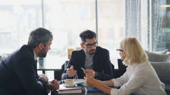Executivos sentados ao redor de uma mesa participam de uma reunião corporativa.