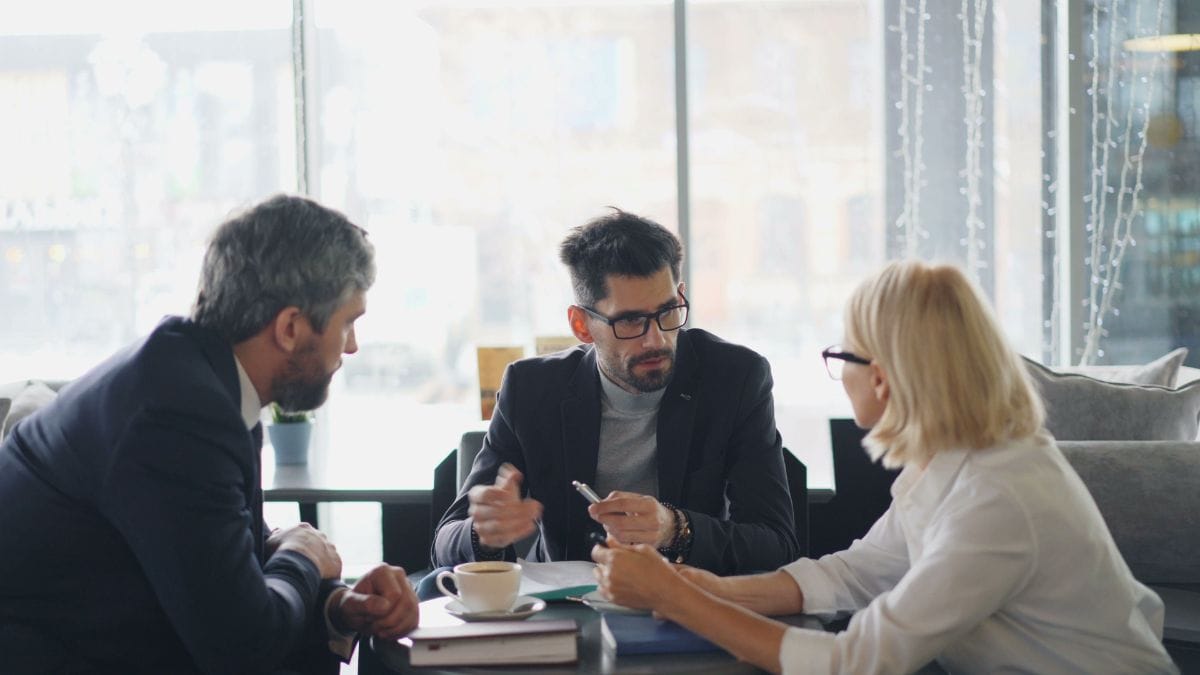 Executivos da empresa sentados ao redor de uma mesa participam de uma reunião corporativa.