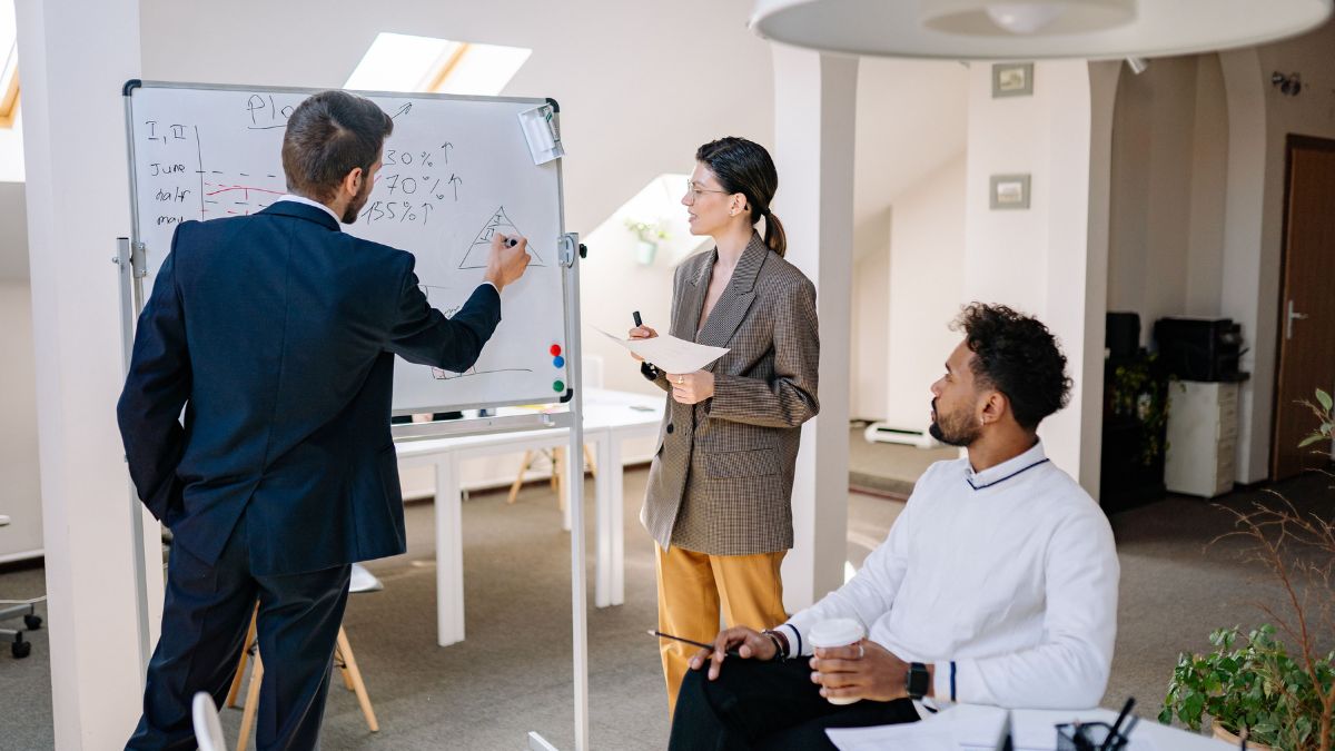 Executivos da empresa reunidos em uma sala de reunião escrevem informações em um quadro branco enquanto discutem estratégias de trabalho.