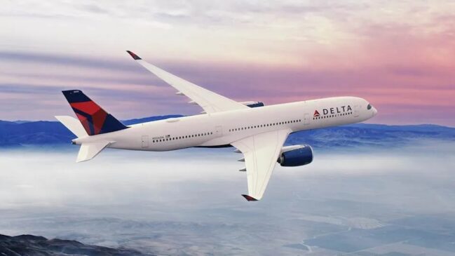 Fotografia institucional de uma aeronave comercial da companhia Delta Air Lines em pleno voo acima de uma camada de nuvens e montanhas ao entardecer. O avião de grande porte, predominantemente branco, exibe a palavra "Delta" acompanhada do logotipo em vermelho e azul na parte dianteira da fuselagem.