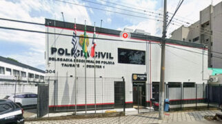 Fotografia de rua da fachada da Delegacia Seccional de Polícia de Taubaté (Deinter 1), da Polícia Civil do Estado de São Paulo. O prédio de fachada branca e detalhes em vermelho e preto tem o número 304 e o letreiro principal "POLÍCIA CIVIL" e "DELEGACIA SECCIONAL DE POLÍCIA TAUBATÉ - DEINTER 1". À frente, há mastros com as bandeiras do Brasil, São Paulo e Taubaté. Um pino de localização do Google Maps está no topo. À direita, placa indicando "Plantão 24h"