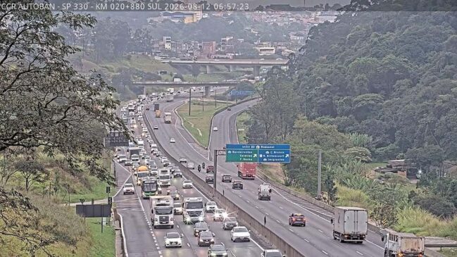 Imagem de câmera de monitoramento viário no km 20 da Rodovia Anhanguera (SP-330), sentido São Paulo (Sul). À esquerda, as faixas de rolamento exibem intenso fluxo de veículos com fila de carros, ônibus e caminhões em trânsito lento. À direita, as faixas de acesso ao Rodoanel Mário Covas (Saída 22) apresentam tráfego normal. Ao centro, destaca-se uma grande placa azul de sinalização rodoviária sobre a pista e, no topo superior esquerdo, um banner com dados técnicos da concessionária CCR AutoBān.
