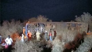 Fotografia noturna de um autocarro de passageiros tombado de lado fora da estrada numa área de mato na Bahia, com equipas de resgate e bombeiros a prestar socorro no local