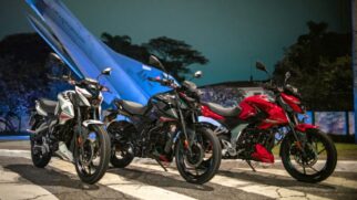 Fotografia de três motocicletas Bajaj Pulsar N150 nas cores branca, preta e vermelha alinhadas lado a lado à noite, posicionadas em frente a uma aeronave monumento da Força Aérea Brasileira iluminada em azul ao fundo