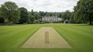 Imagem limpa em 16:9 de um pitch de críquete vazio no centro do quadro, gramado cuidado e wickets alinhados, sugerindo a ampliação em estate rural britânica sem pessoas e sem marcas gráficas.