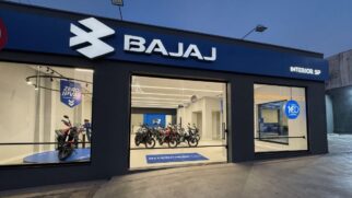Fotografia de fachada de uma concessionária da marca Bajaj com vidraças transparentes, exibindo motocicletas expostas no show-room e iluminação noturna
