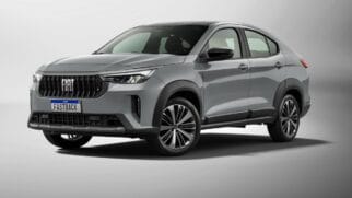 Fotografia de estúdio em ângulo três quartos dianteiro de um SUV cupê Fiat Fastback na cor cinza. O veículo possui grade frontal escura com o logotipo "FIAT" ao centro, faróis afilados em LED, teto e retrovisores pretos e rodas de liga leve diamantadas sobre fundo neutro claro
