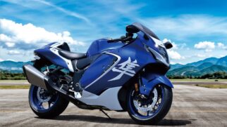 Motocicleta desportiva Suzuki Hayabusa azul e branca vista de perfil numa pista, com ideograma japonês na carenagem e céu azul ao fundo